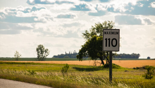 A street sign reads "Maximum 110" on a road in the praries