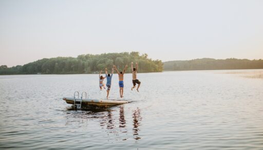 Kids jumping off a floating dock into a lake.