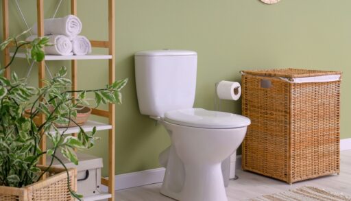 Toilet in a green bathroom next to a wicker basket and shelf.