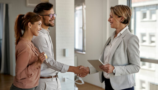 Female real estate agent shaking hands with a young couple.