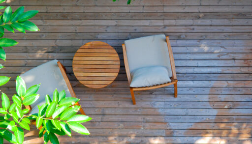 Overhead view of a wooden deck with two grey deck chairs next to a green tree.