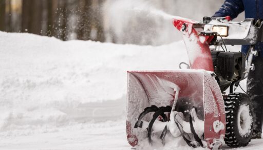 Close-up of a red snow blower clearing snow from a pathway.