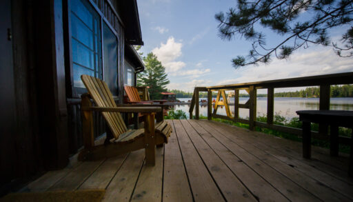 Side view of a deck next to a lake with two Adirondack chairs.