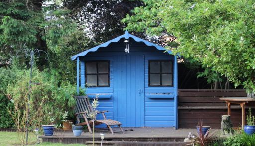 blue-shed-surrounded-by-trees-with-a-chair-in-front