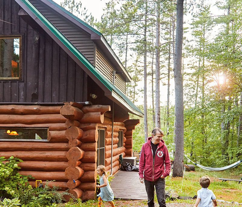 Stephen Gardner outside his log cabin with kids running around