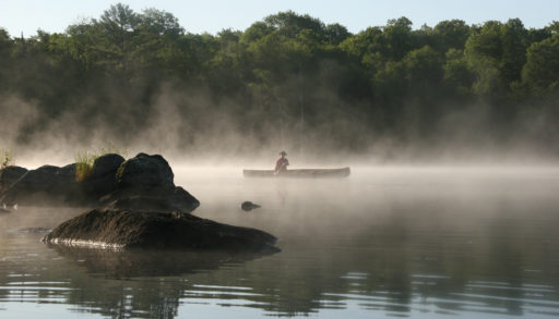 A person canoeing on a Misty Lake in the Haliburton Highlands.
