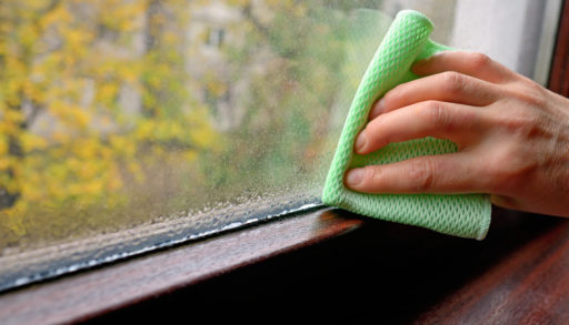 A hand wiping a wet windowsill with a green cloth