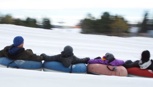 People holding onto each other while snow tubing
