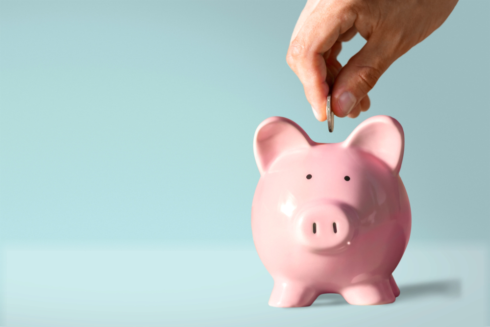 a hand putting a coin in a piggy bank on a blue background, budget