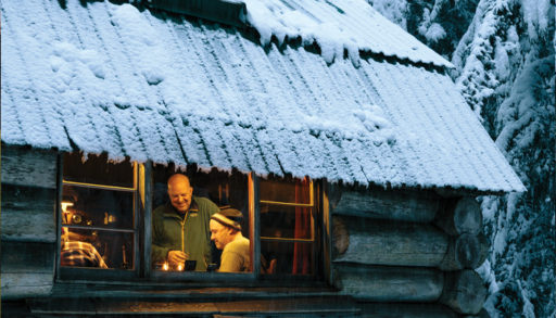 Several men gathered in a lit, snowy cabin