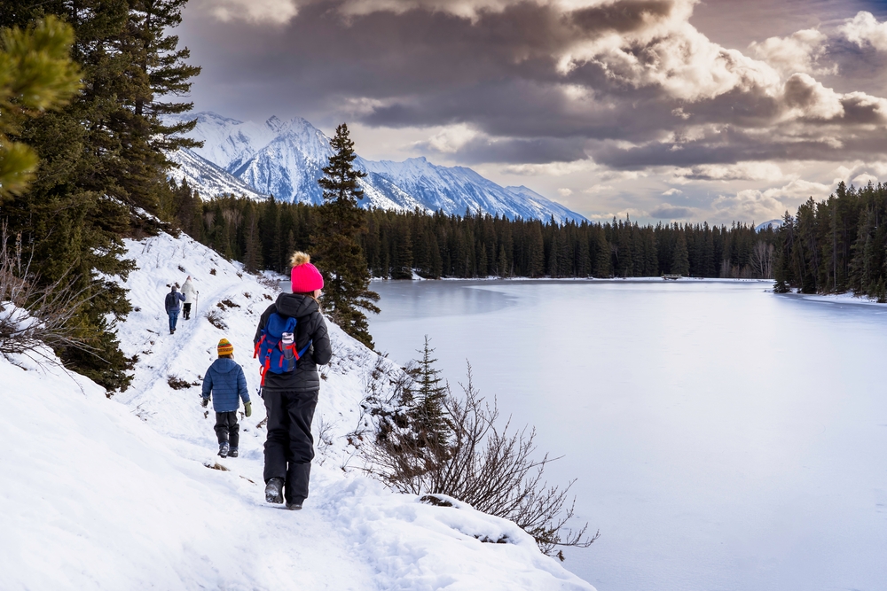 A group of people walking on a winter hiking trail along Johnson Lake in Banff National Park Canada