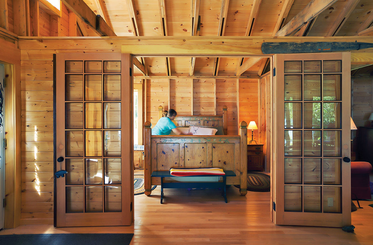 Bedroom inside the cottage with open glass doors and someone making the bed