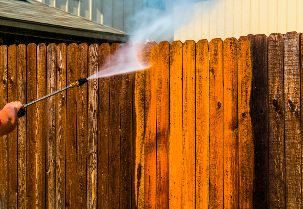 Someone pressure-washing a stained fence