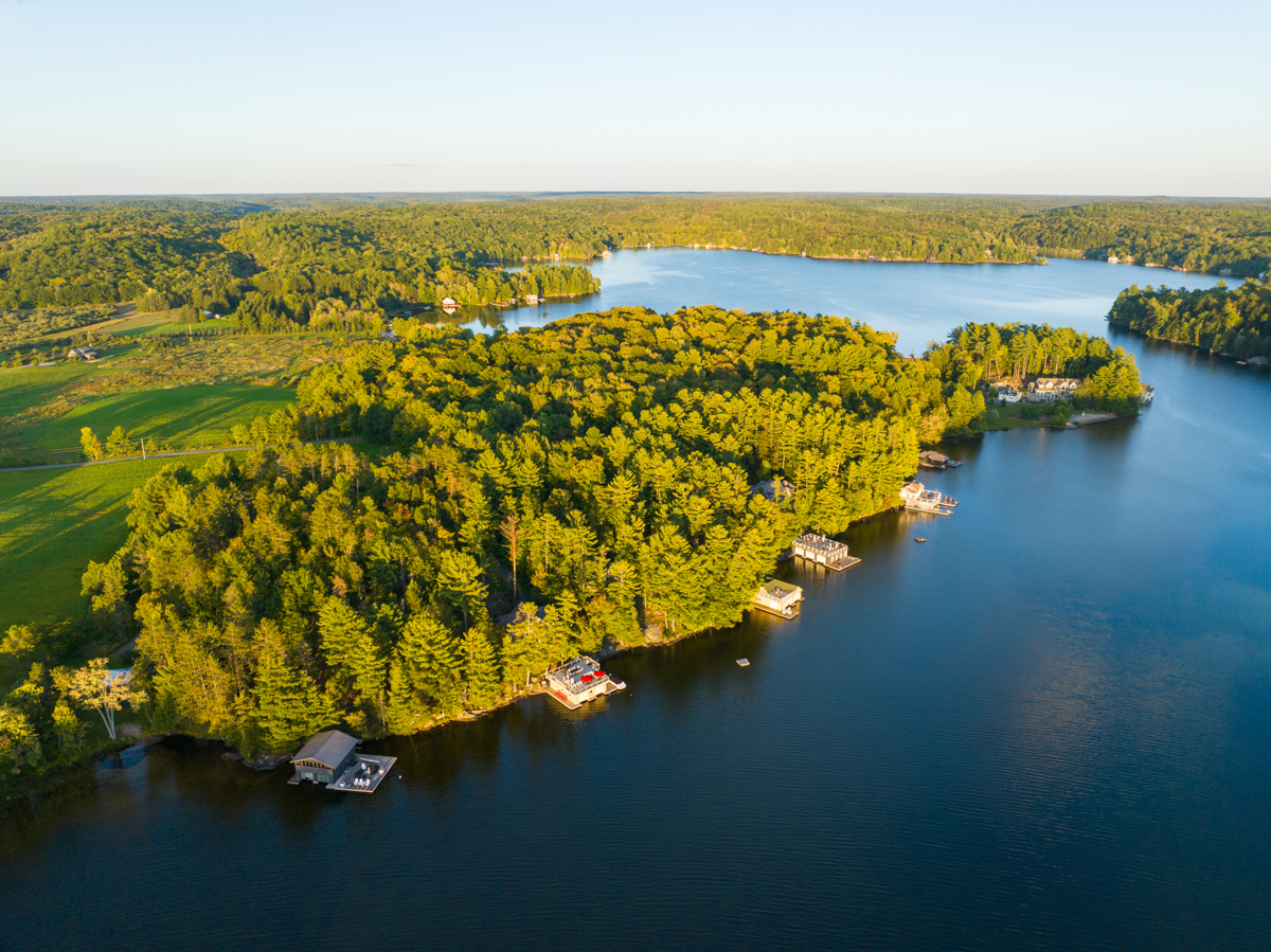 Overhead view of a lake with a shore lined with green trees and big cottages.