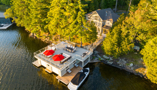 A large boathouse with a rooftop deck extends into a lake from a tree-lined shore.