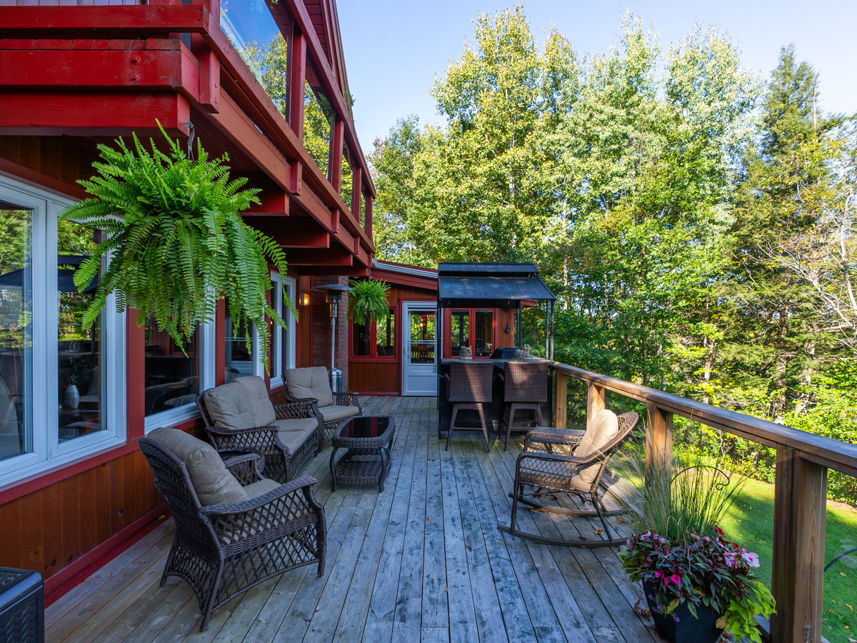 A deck with lots of outdoor furniture extends off the back of a cottage.