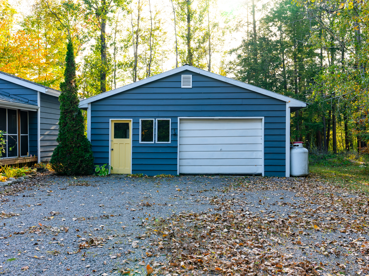 A detached garage, painted blue with a yellow entrance door and a white garage door.