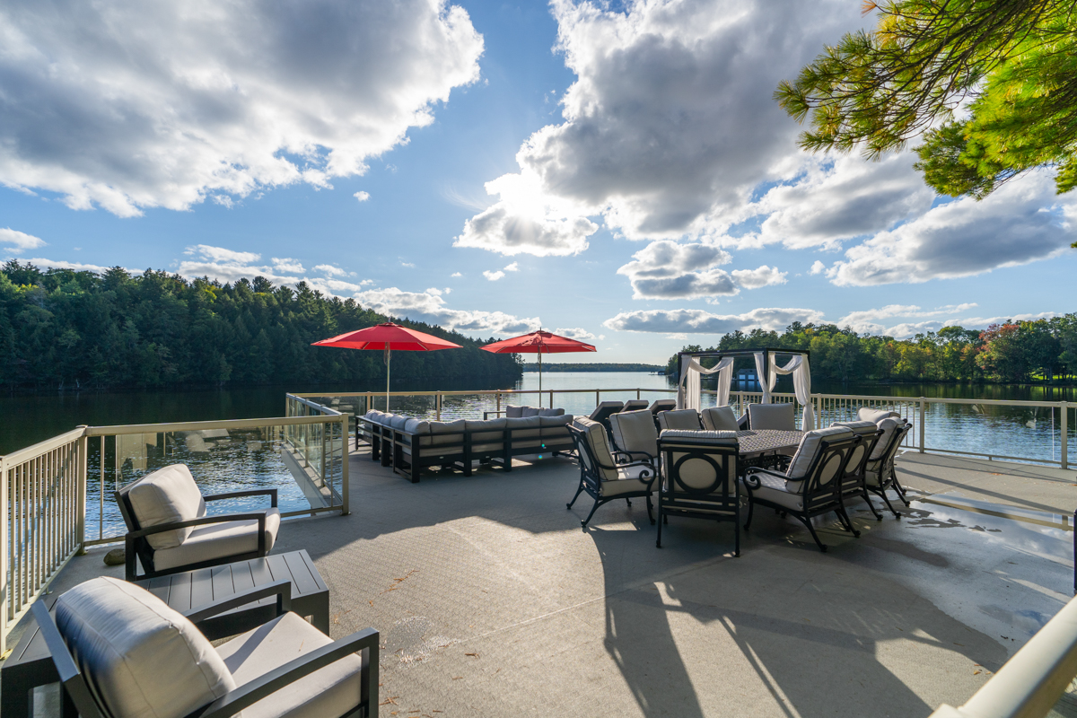 A large rooftop deck with outdoor living and dining furniture, looking out over a lake.