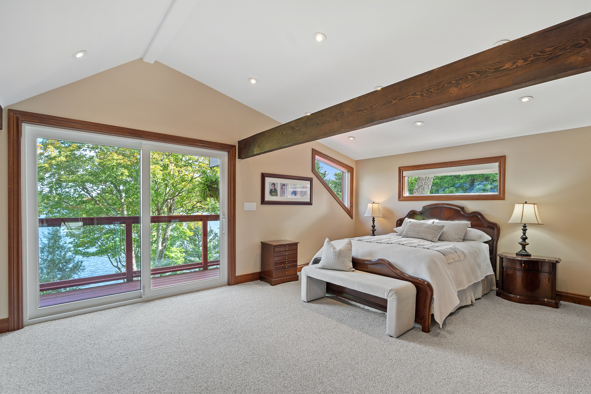 A huge bedroom with a large bed, an exposed wooden beam in the ceiling, carpeted floors, and double doors that lead out to a balcony.