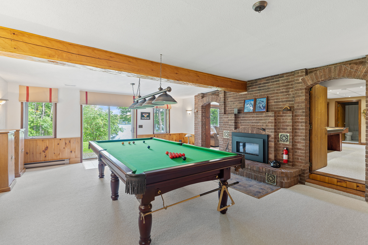 A rec room with a pool table, a fireplace, and double doors that open to a grassy outdoor space.