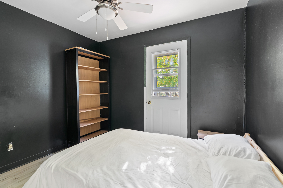 A small bedroom with black walls, a bed, and a bookcase.