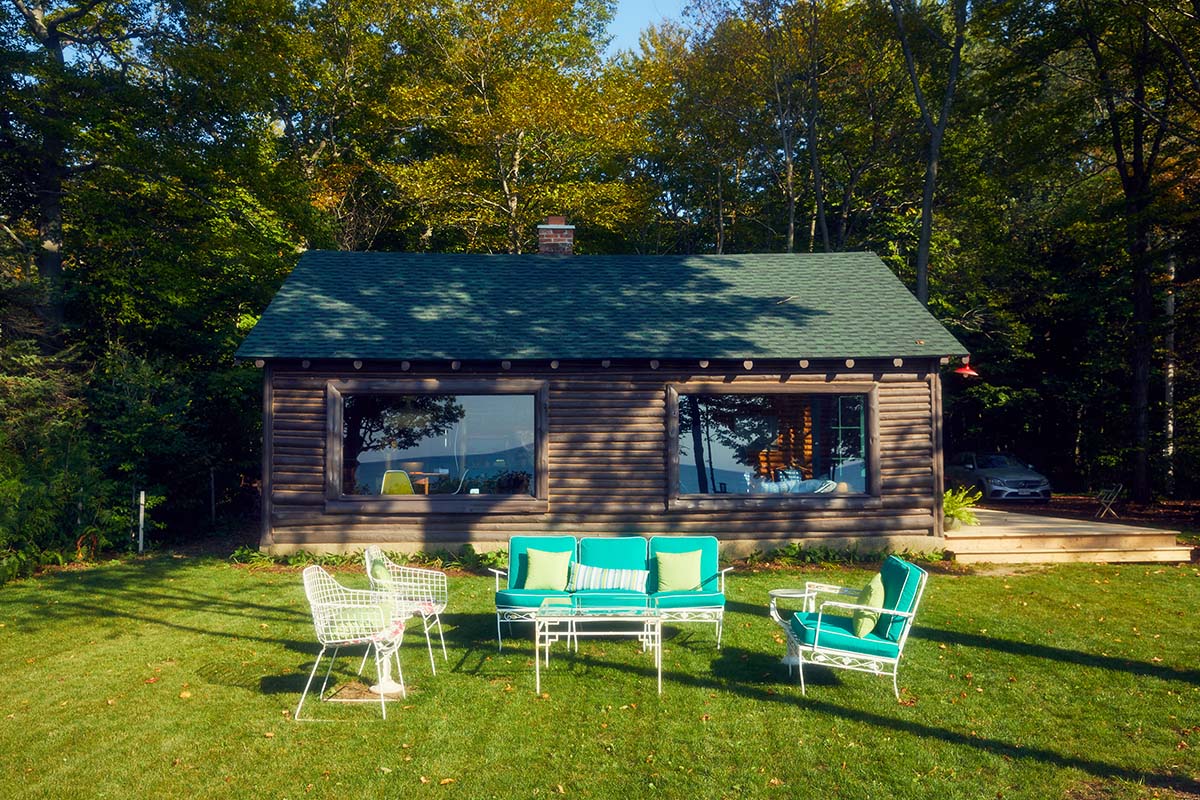 an exterior shot of the back of a cottage with a deck and patio furniture on the lawn