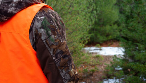 man wearing hunter orange vest in the woods