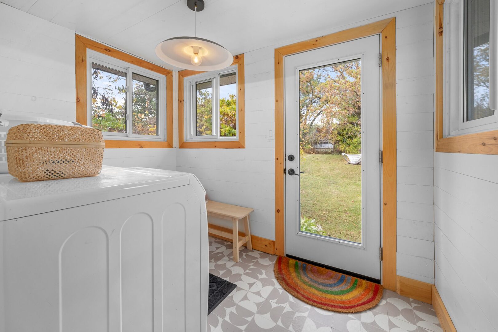 A small laundry area with a door leading to the backyard. A rainbow doormat sits in front of the door.