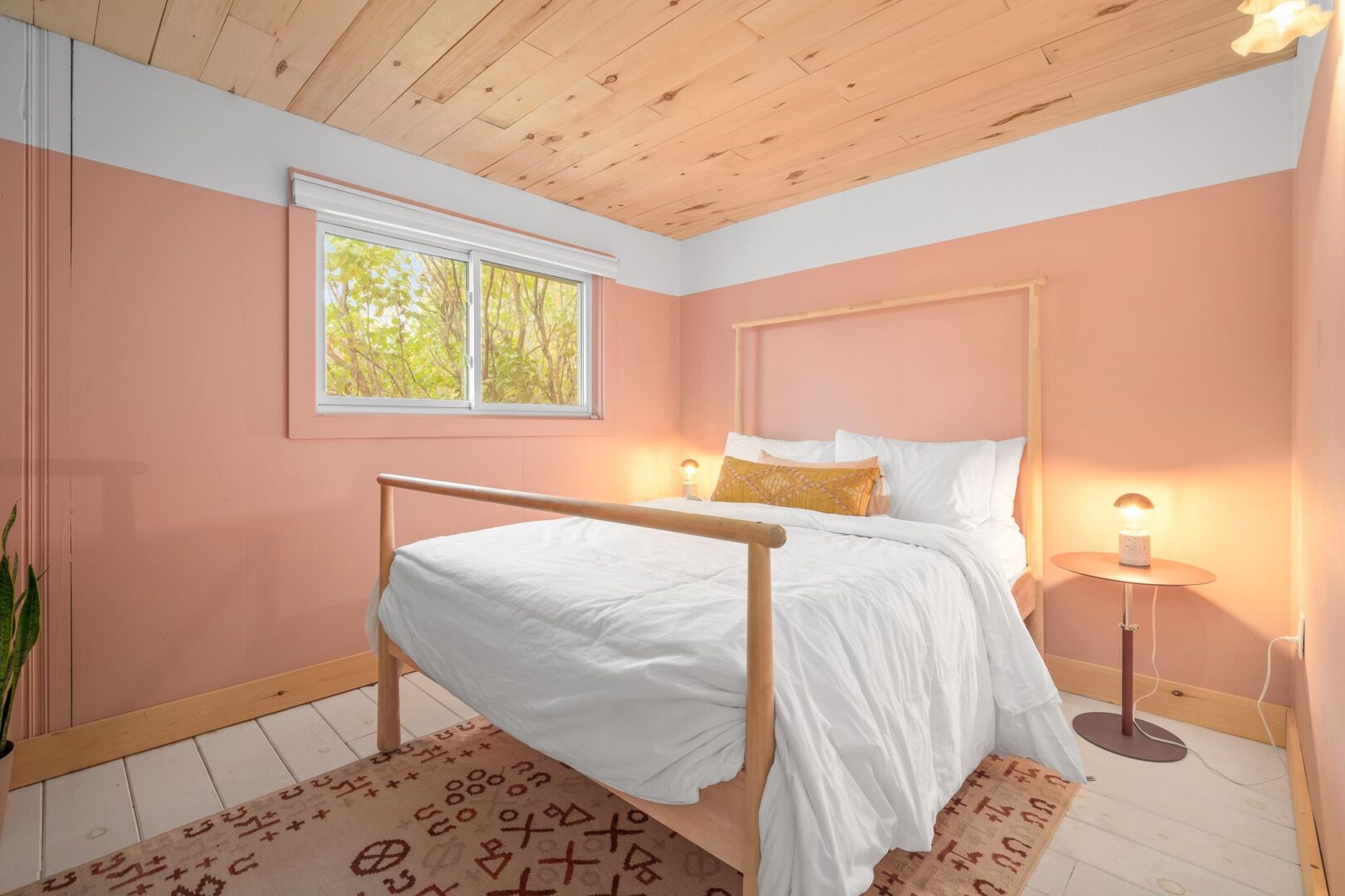 A big, bright bedroom with a large bed, a wood-panelled ceiling, and pink walls.