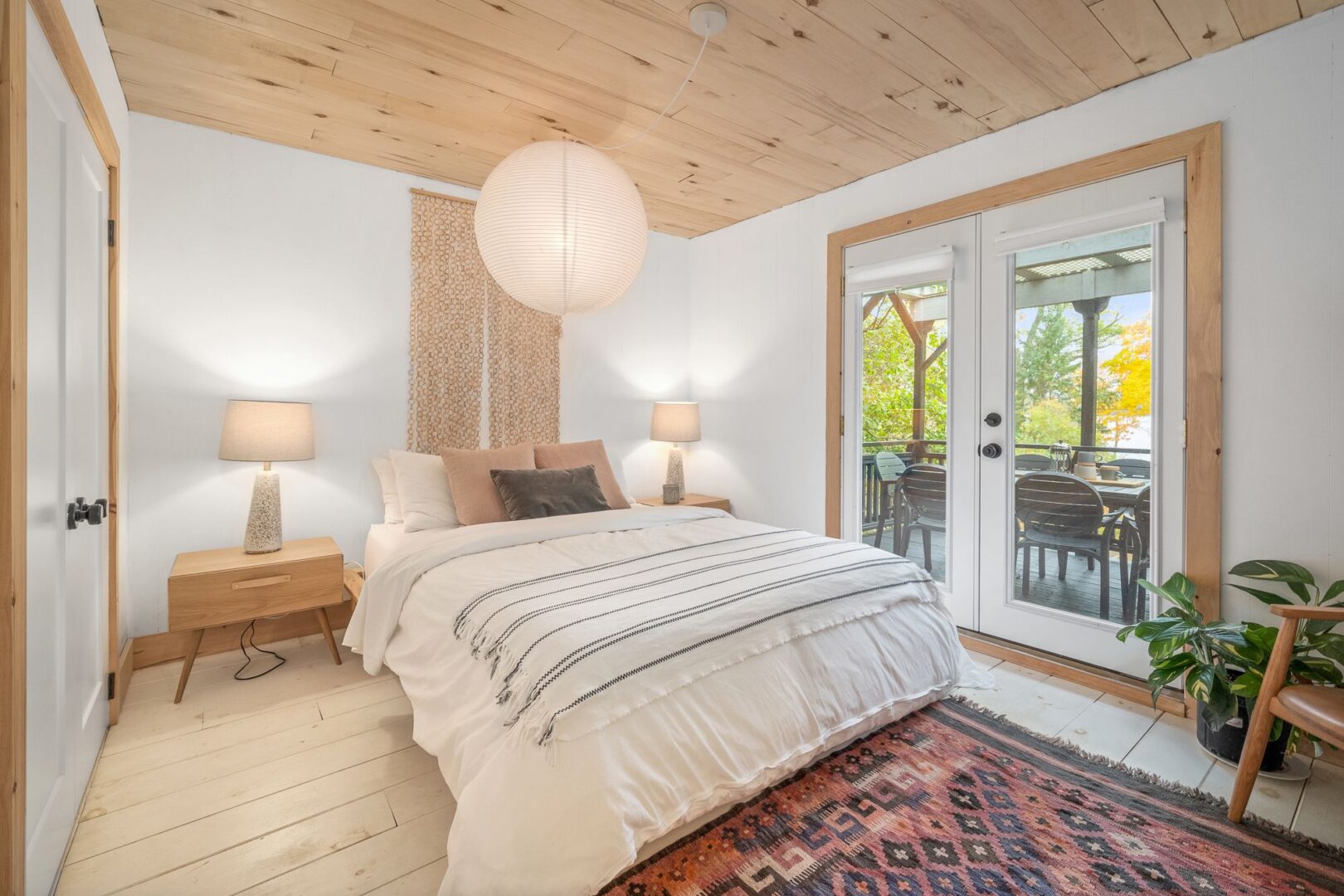 A big, bright bedroom with a large bed, a wood-panelled ceiling, and double glass doors leading to a deck.