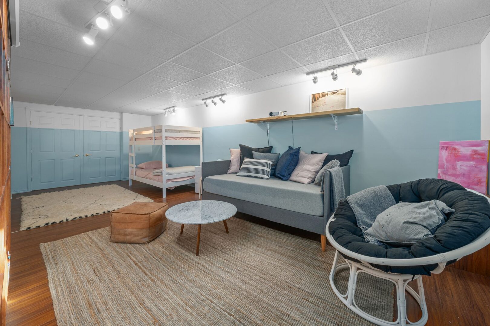 A finished basement area with lots of seating, light blue walls, and bunk beds.