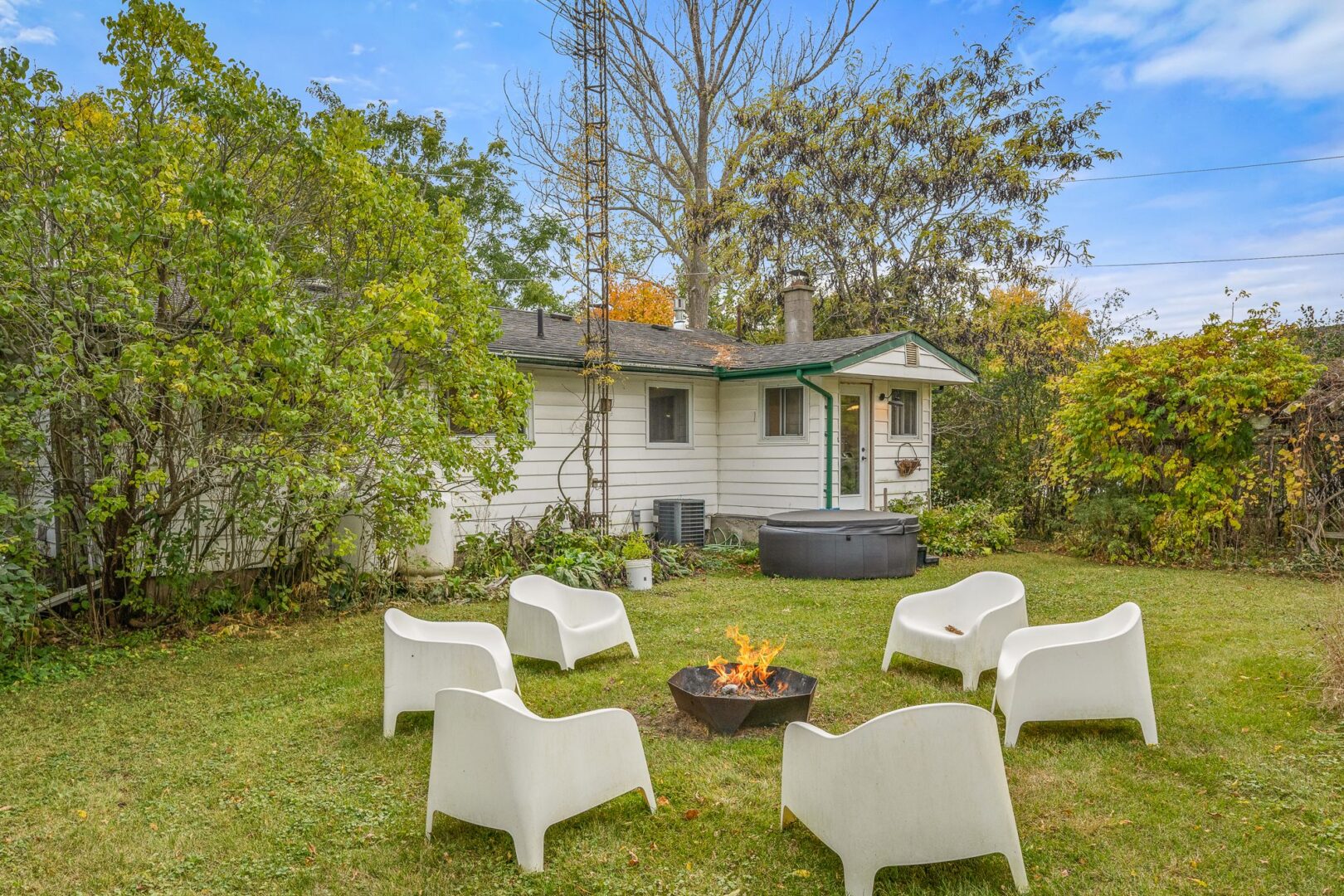 Chairs sit around a fire pit in an open, grassy outdoor space in the backyard of a small bungalow.