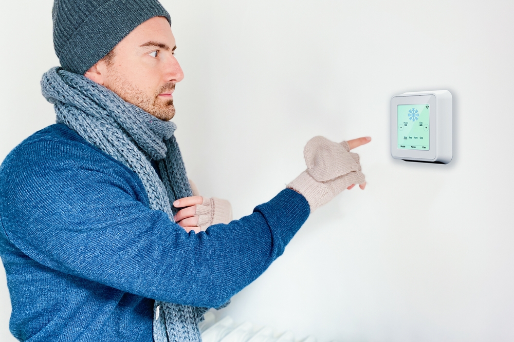 A man adjusting the digital thermostat of a home heating system