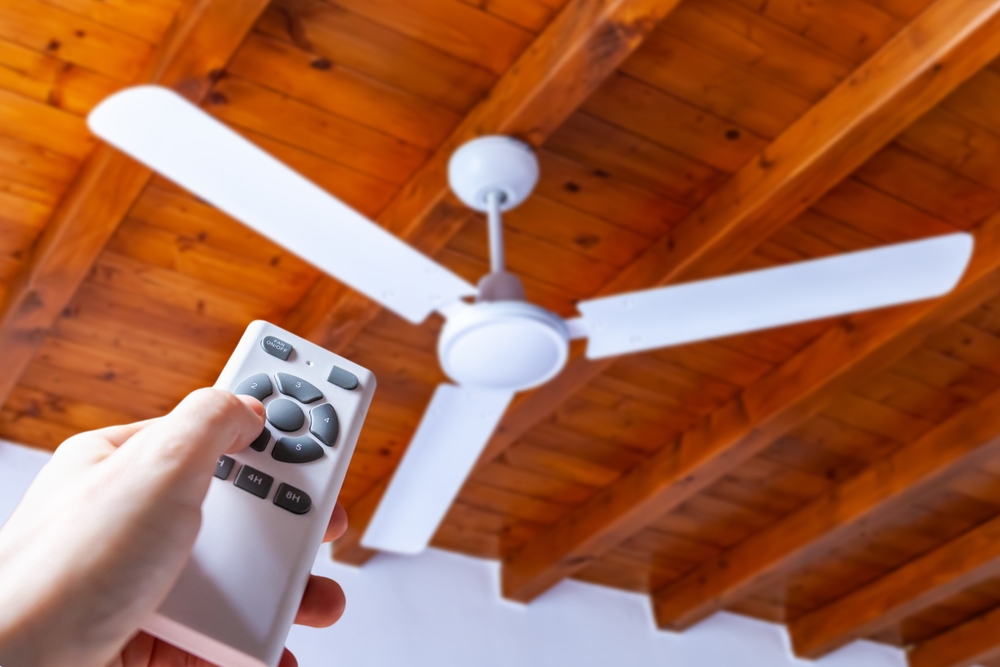 A hand adjusting a ceiling fan via remote control