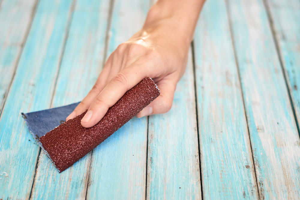 A hand using a piece of sandpaper on a deck