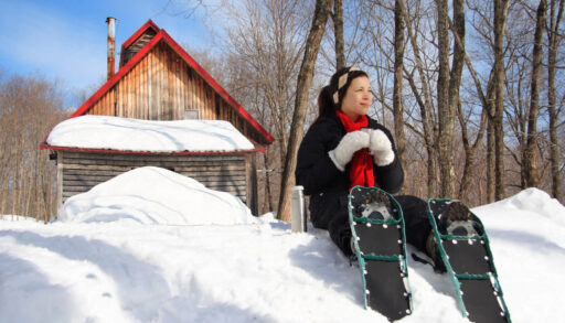 a woman sitting in front of a cabin wearing snowshoes