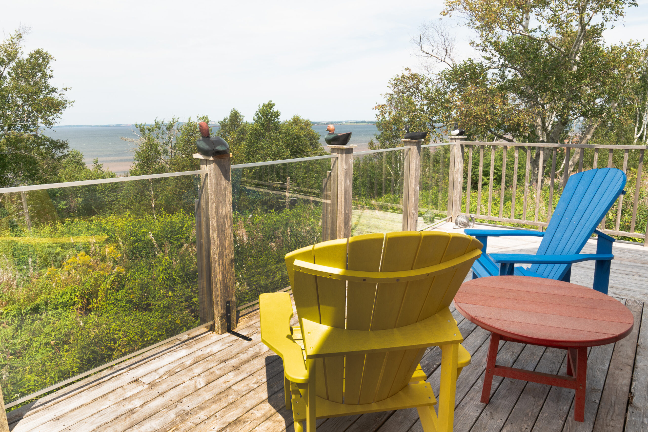 Blue and yellow Muskoka-style chairs sit on a small deck, looking out toward the water.