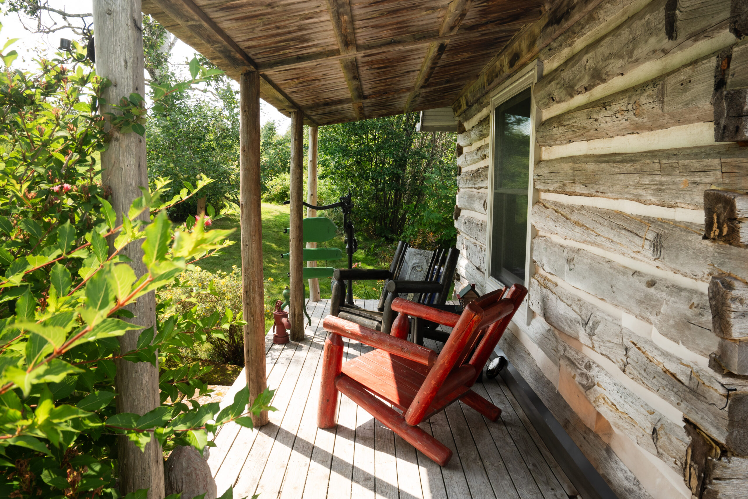 A covered porch on a small log cabin, with two Muskoka-style chairs.