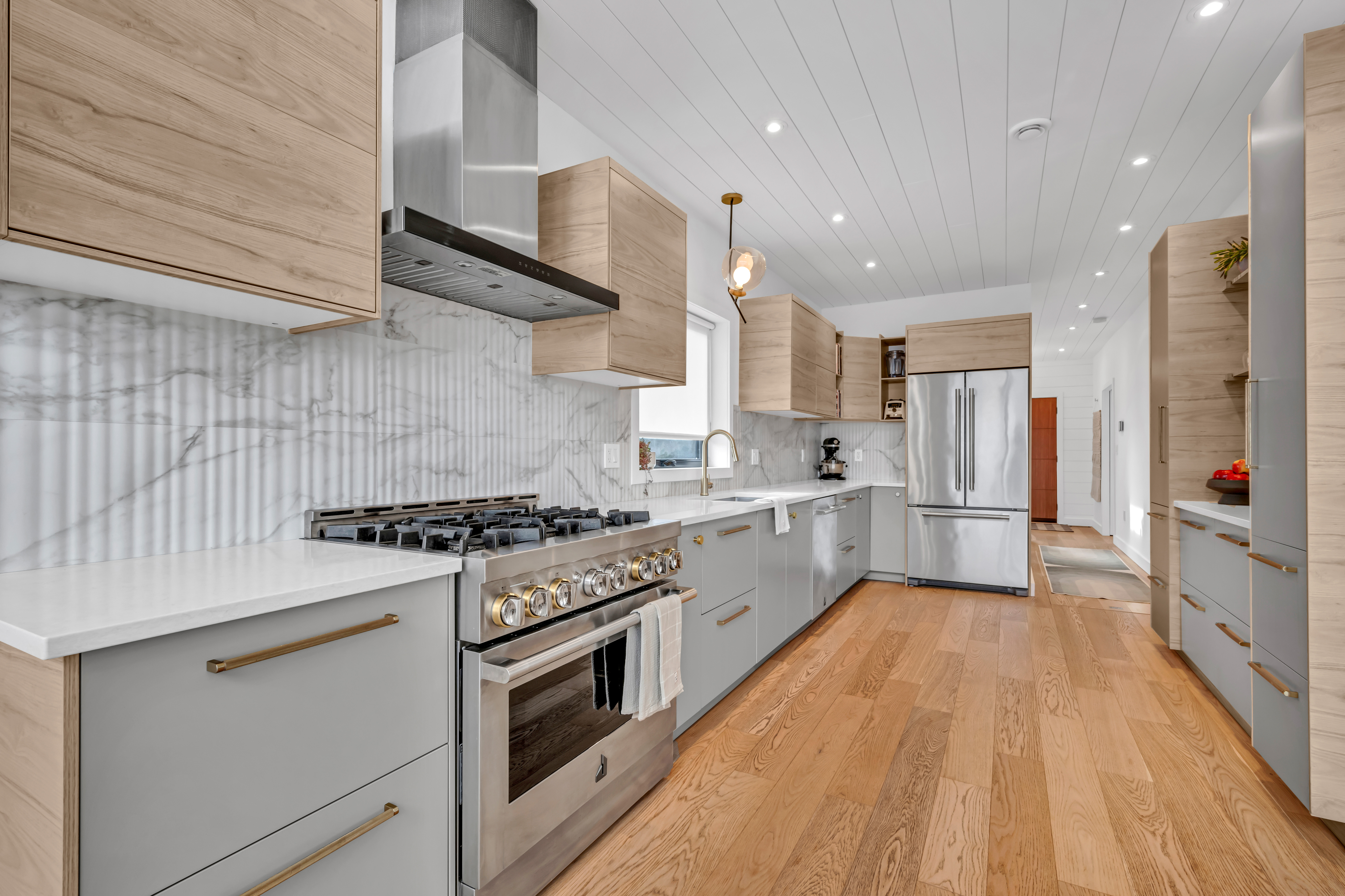 A big, bright, modern kitchen with light gray cabinetry, stainless steel appliances, light hardwood flooring, and lots of countertop space.