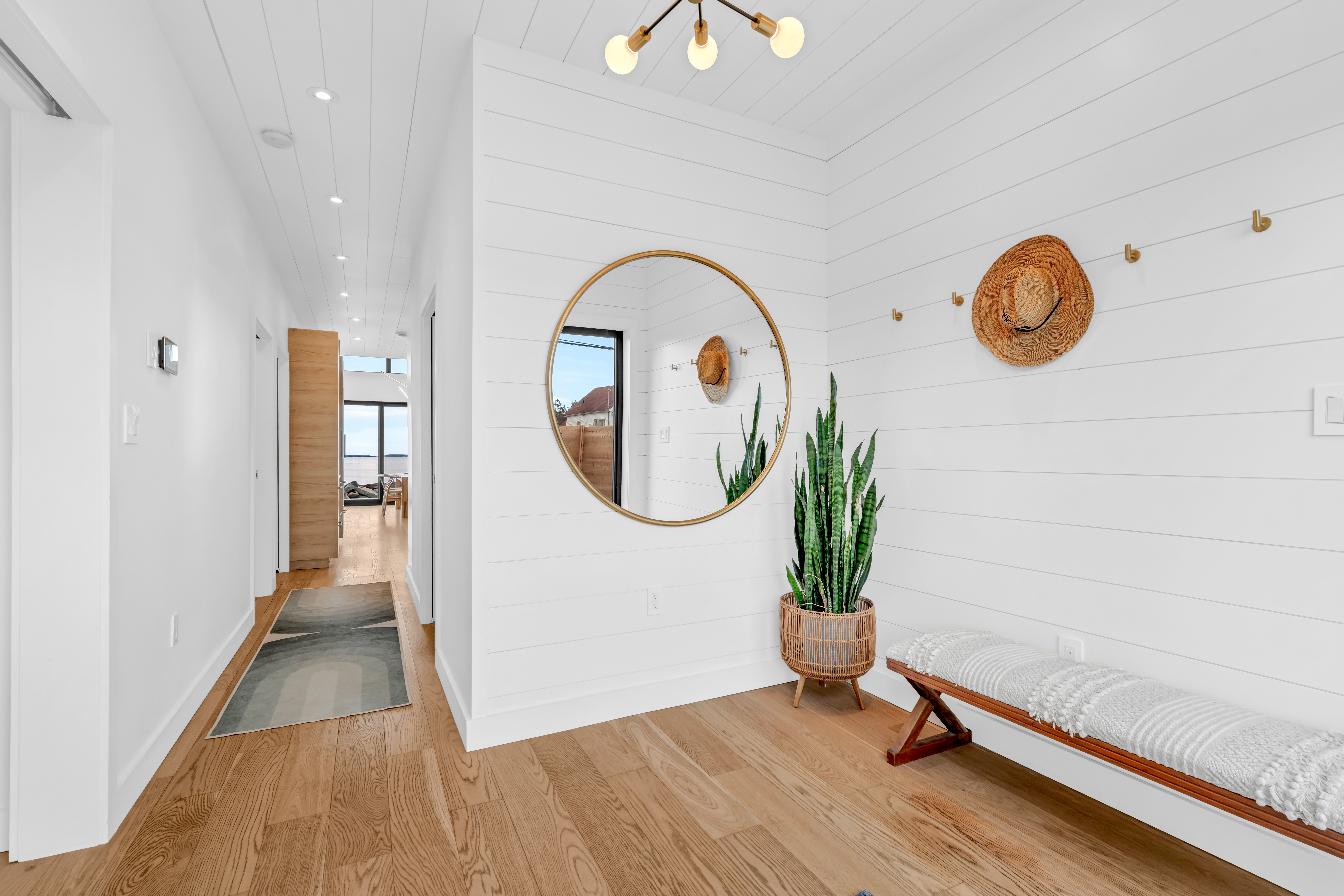 A bright front entryway with white-painted shiplap walls and ceiling. A narrow hallway leads into the home beyond.