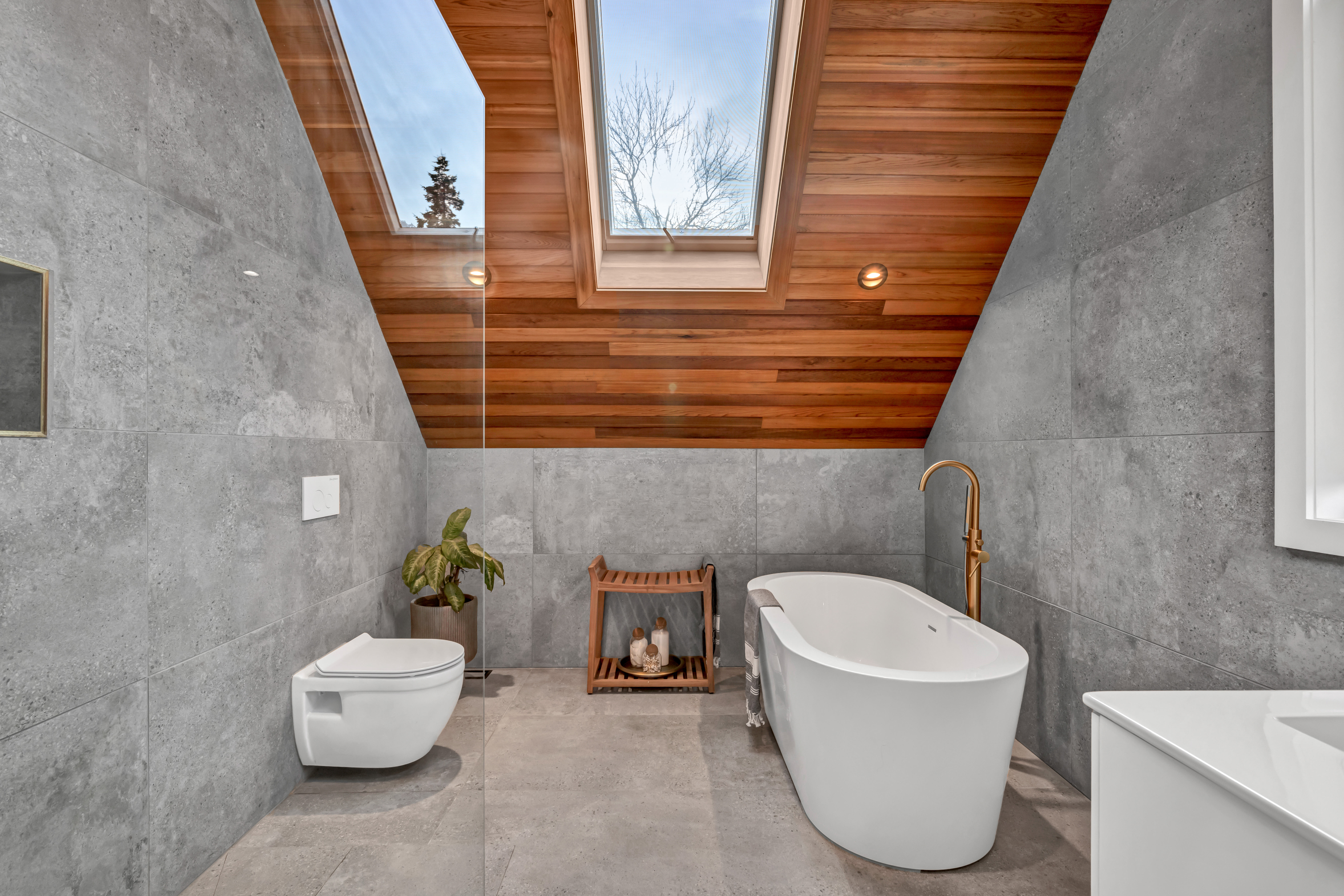 A bright bathroom with a soaker tub, a toilet, and a wood-panelled ceiling with a skylight.