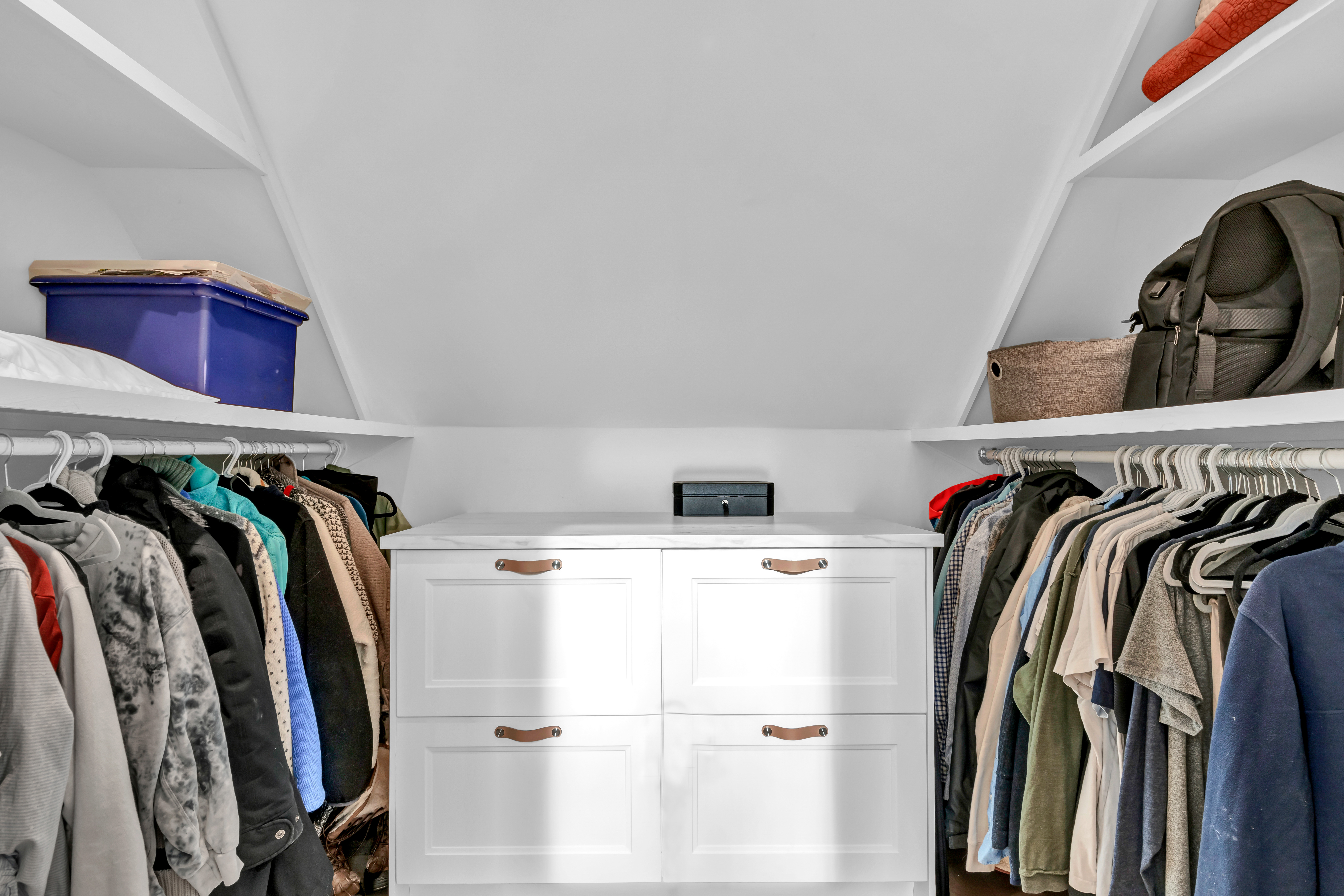 A walk-in closet with a short dresser flanked by hanging racks with shelves above.
