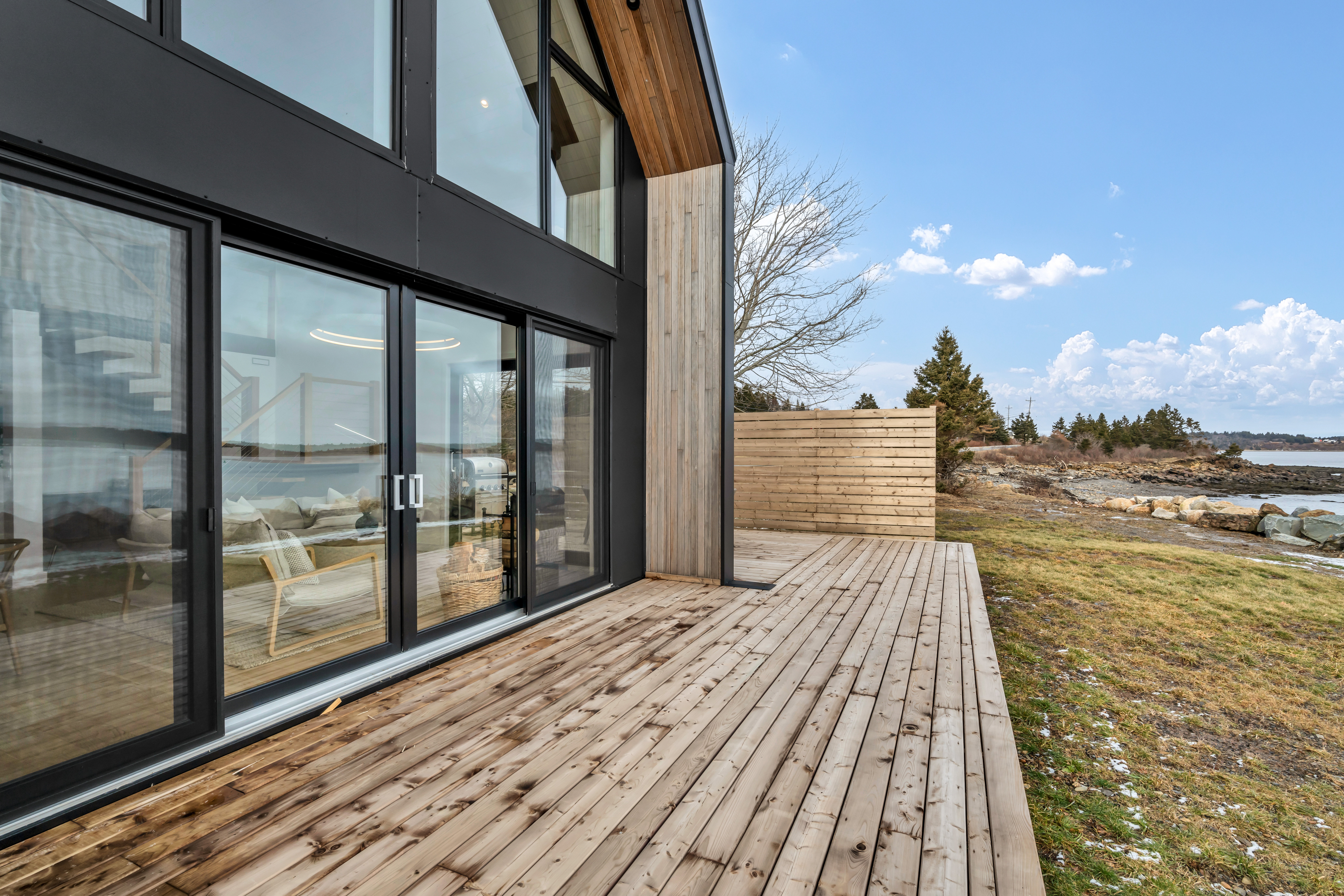 A wooden deck extends off the back of a modern oceanfront home with big windows.