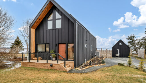 A modern, two-story waterfront home with black siding and a rust-orange door.