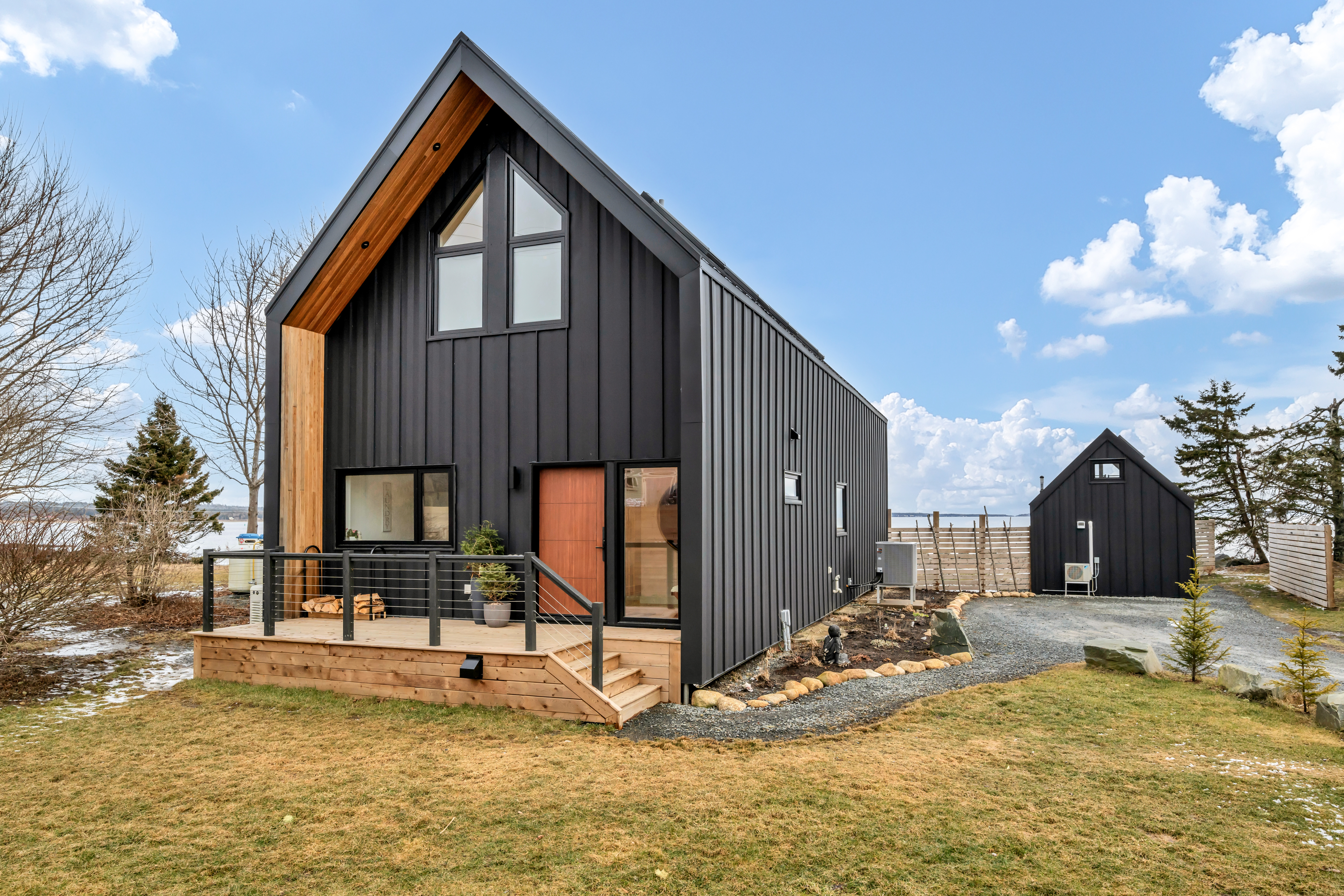 A modern, two-story waterfront home with black siding and a rust-orange door.