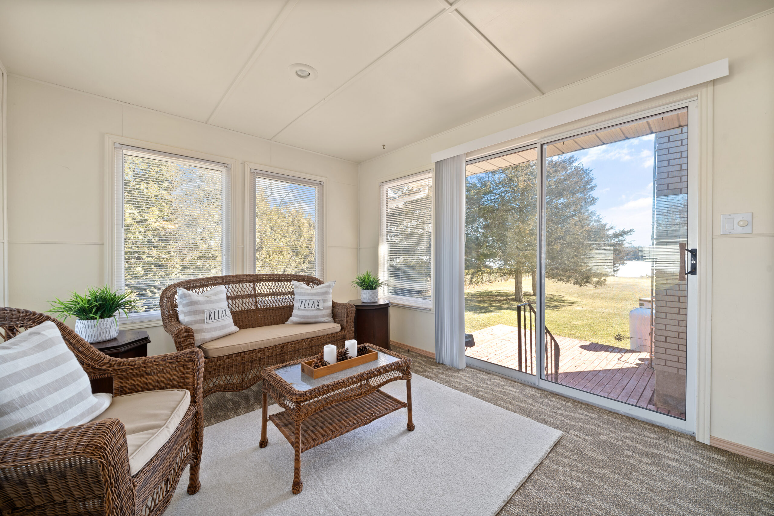 A sunroom with big windows and wicker furniture. Double glass doors lead out to a small porch.
