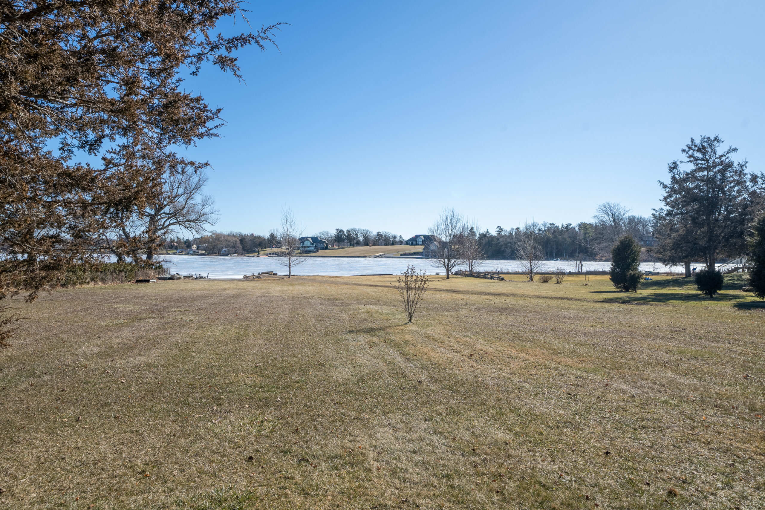 A wide, grassy yard leads to a waterfront area.