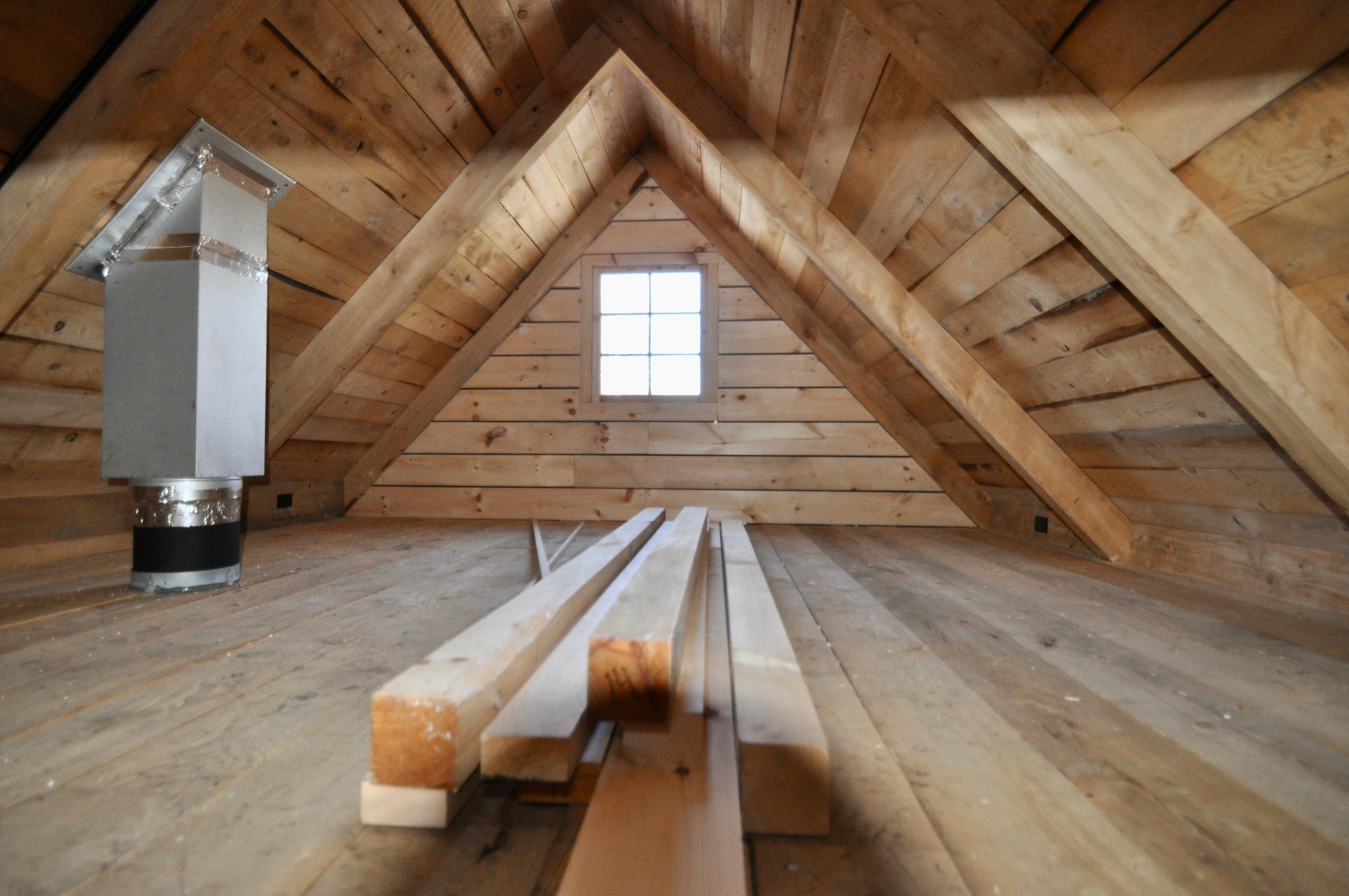 A loft space in a timber frame cabin, with a peaked ceiling and a big window.