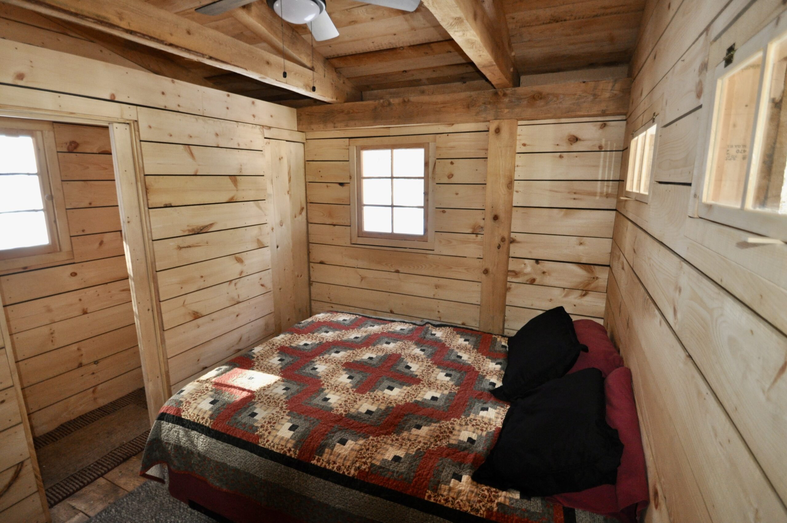 A small, simple bedroom in a wood cabin, with a big bed. Windows let in natural light.
