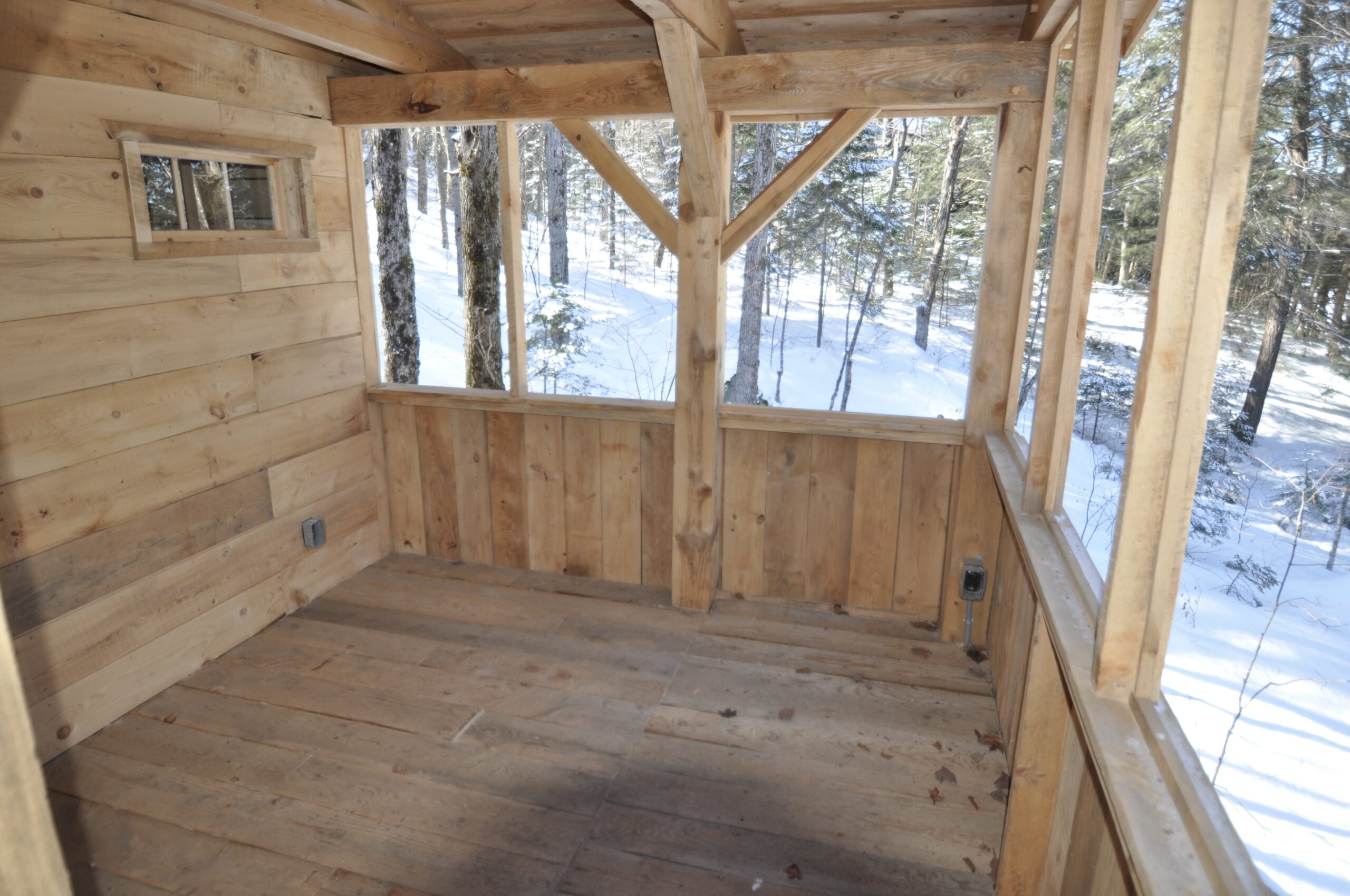Interior of a spacious screened-in porch on a wooden cabin.